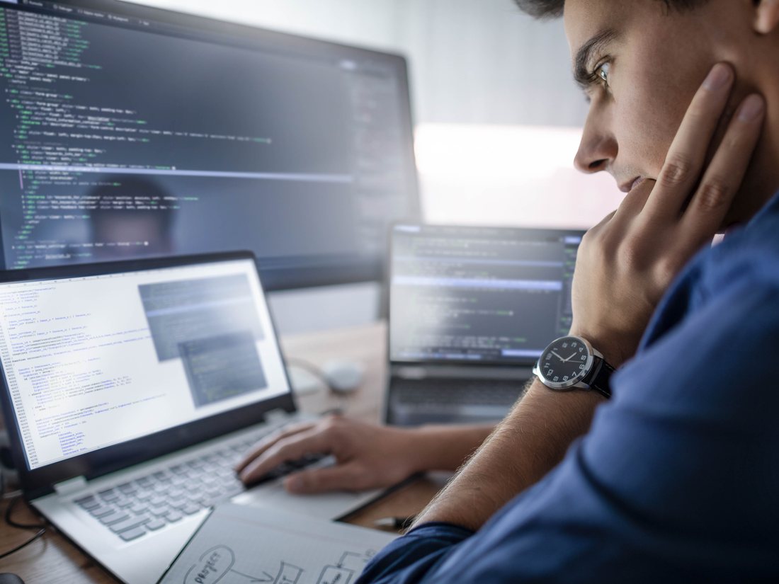 A software developer working across a laptop and two monitors of code